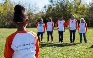 Child wearing a Cornerstones of Care "Together We Can" shirt looking at adults in the distance.